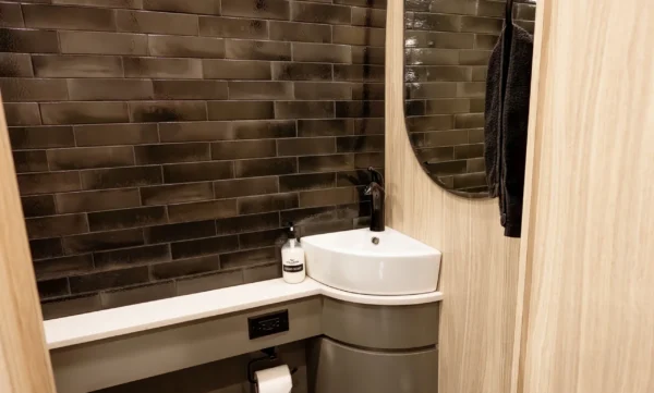 Astro entertainer bus restroom with dark glazed tile wall, corner vessel sink, oval mirror and toilet