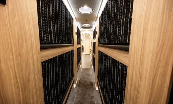 Sleeper bunks along the Astro entertainer bus hallway with patterned privacy curtains, wood trim and carpet runner