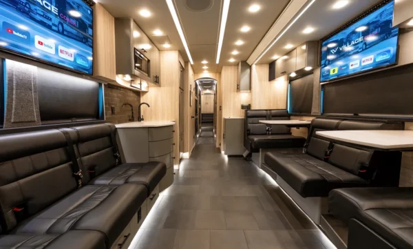 Front lounge of the Astro entertainer coach with black leather seating, dual smart TVs, galley sink and LED-lit tile floor
