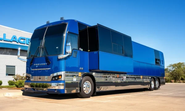Astro Prevost tour bus with its side slide-out extended, metallic blue paint and chrome trim outside Village Coach in Wichita