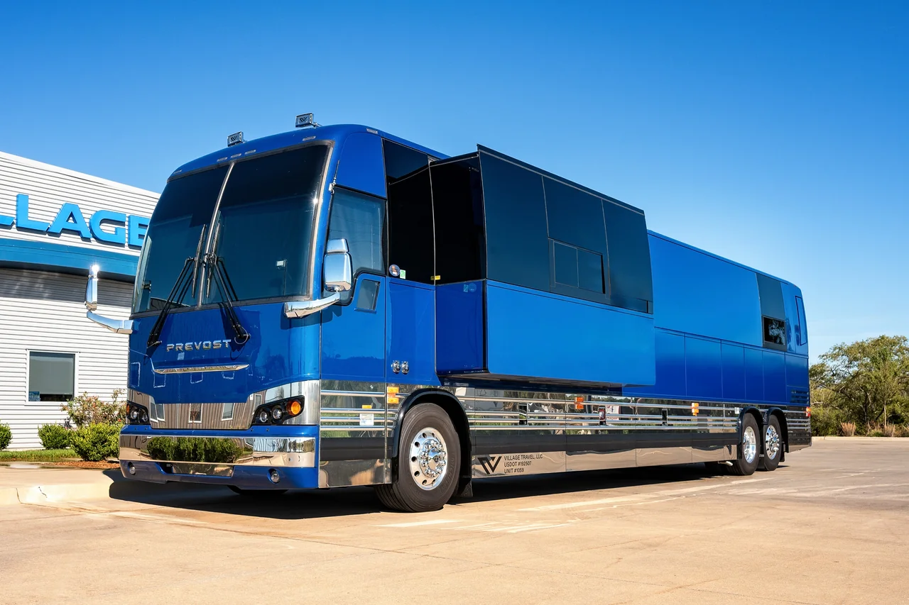Astro Prevost tour bus with its side slide-out extended, metallic blue paint and chrome trim outside Village Coach in Wichita