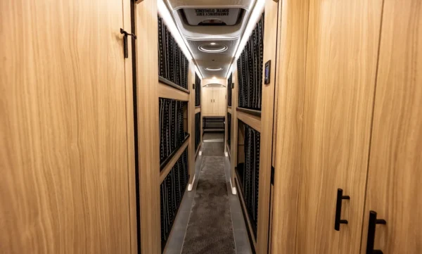Arched wood-paneled entry to the Astro tour bus bunk hallway with curtained sleeper bunks stacked on both sides