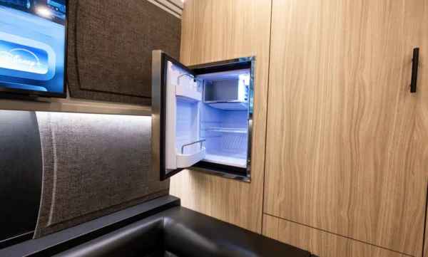 Built-in stainless mini fridge set into wood paneling in the Astro tour bus coach rear lounge